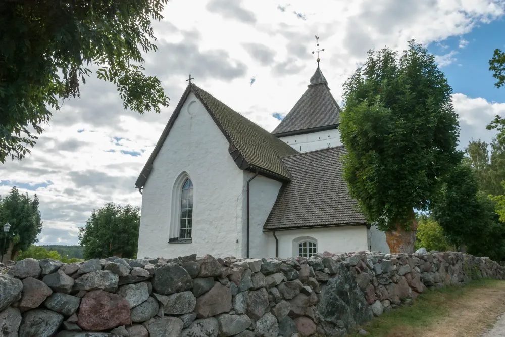 Old church in Hovgarden Sweden with rock wall in front.